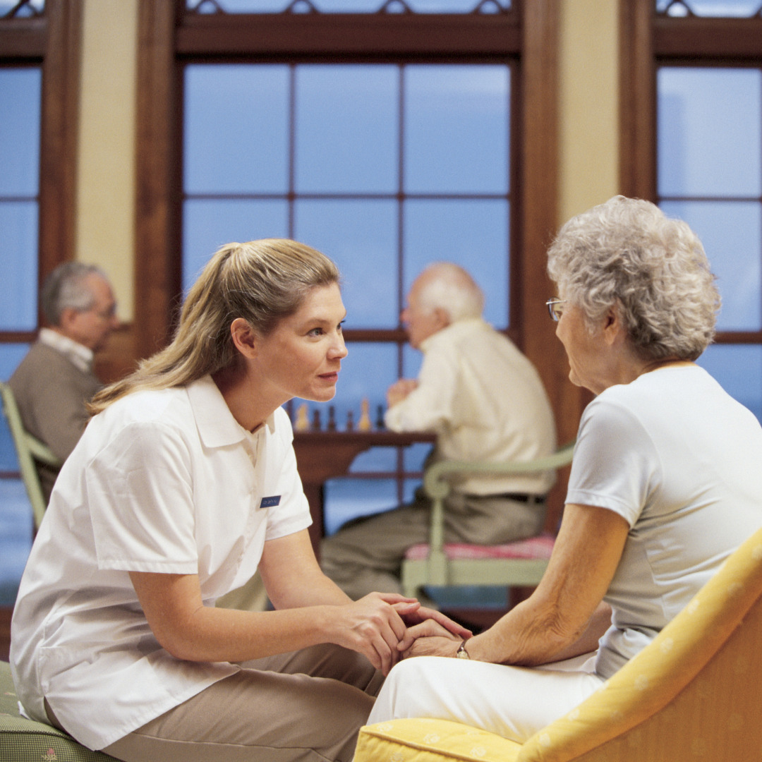 A senior living facility showing a caregiver looking at the face of an elderly woman.